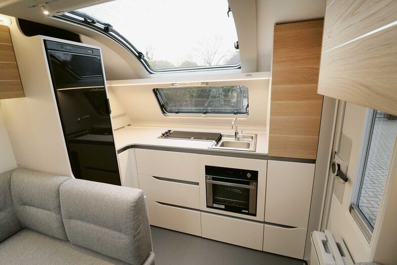 La cuisine placée sous la fenêtre Atrium séduit par son esthétique, ses nombreux rangements et son plan de travail. Le réfrigérateur 140 litres Thetford est à portée de main, sur le côté.